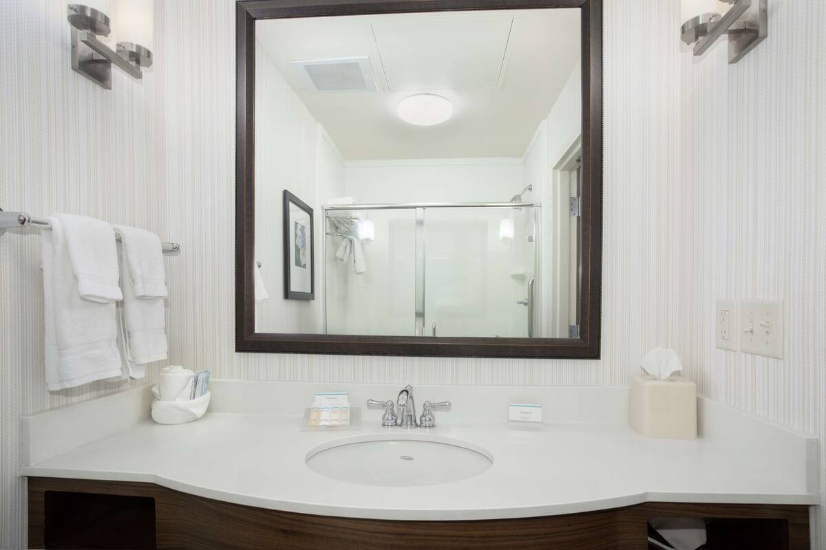 Un baño con un espejo grande, lavamanos blanco y cabina de ducha de vidrio.