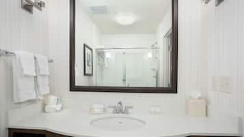 Une salle de bain moderne avec un grand miroir, un lavabo blanc et une cabine de douche en verre.