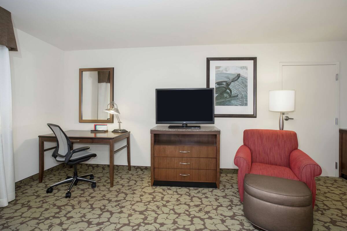 Una habitación de hotel con escritorio, silla, televisión y un sillón rojo.