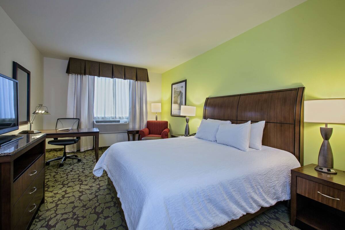 Una habitación de hotel con una cama grande, un escritorio con una silla, un televisor y dos lámparas.