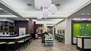 A modern hotel lobby with a bar area, seating, and a reception desk. - Hilton Garden Inn Lincoln Downtown/Haymarket (Lincoln)