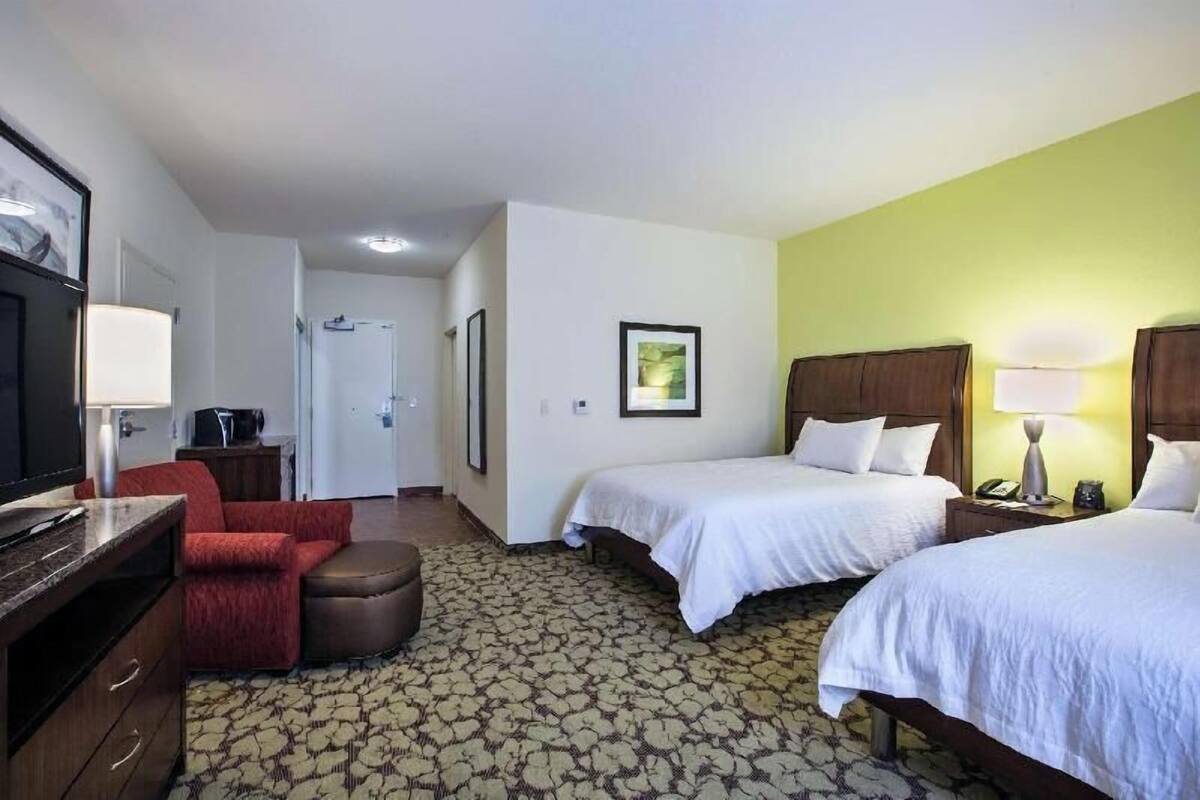 Habitación de hotel con dos camas, televisor, escritorio, silla y alfombra estampada.
