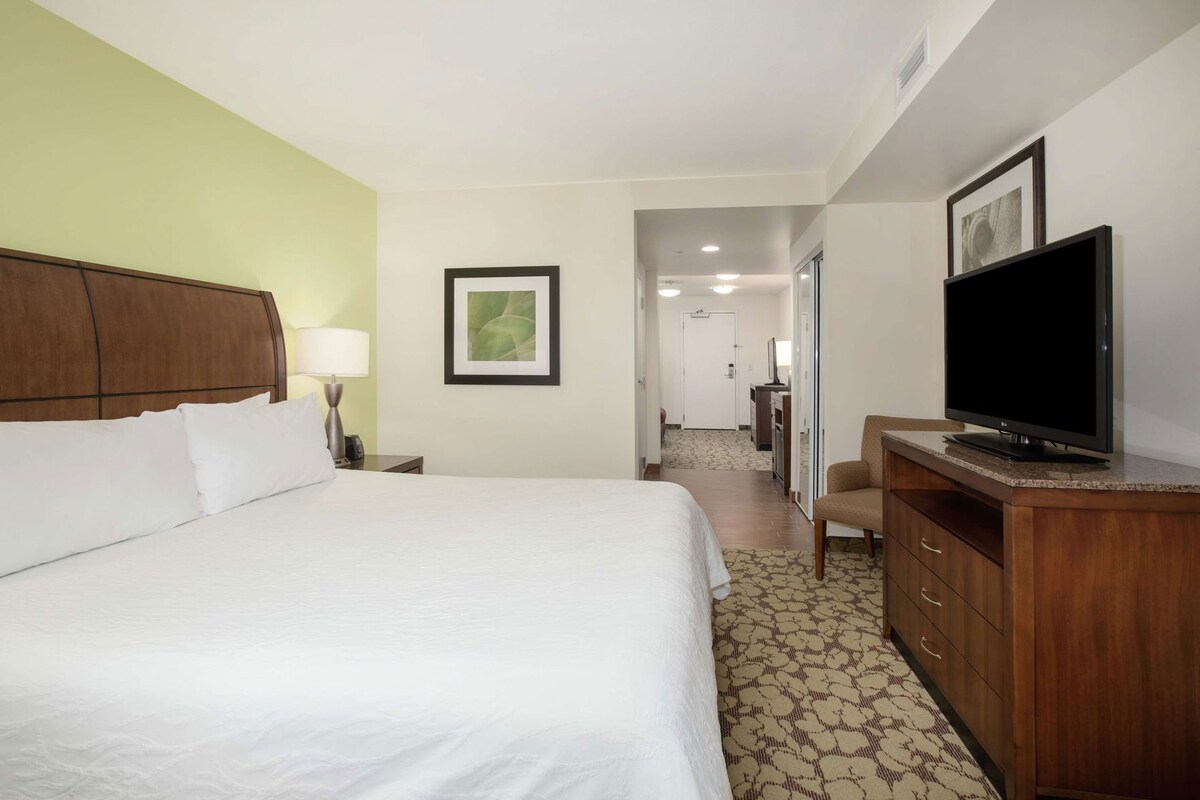 A hotel room with a large bed, a desk with a television, a lamp, and a framed picture on the wall.