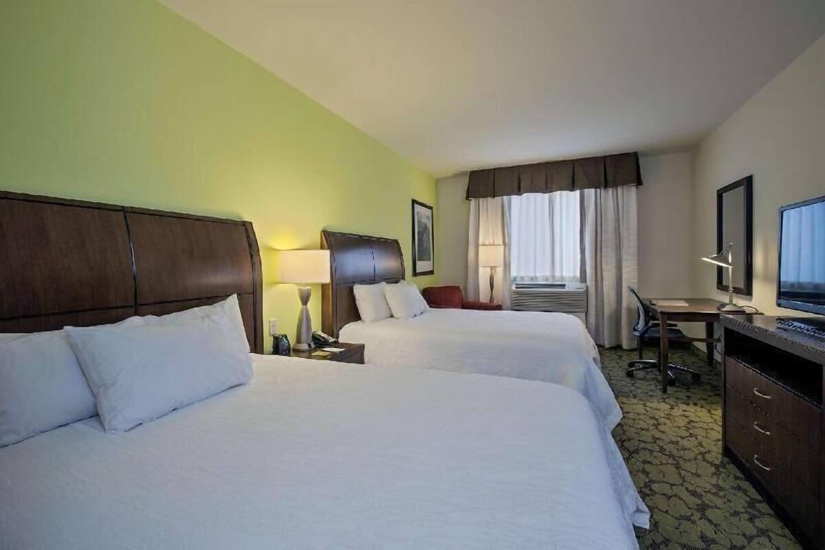 Habitación de hotel con dos camas, un escritorio, una silla, un televisor y una ventana con cortinas.