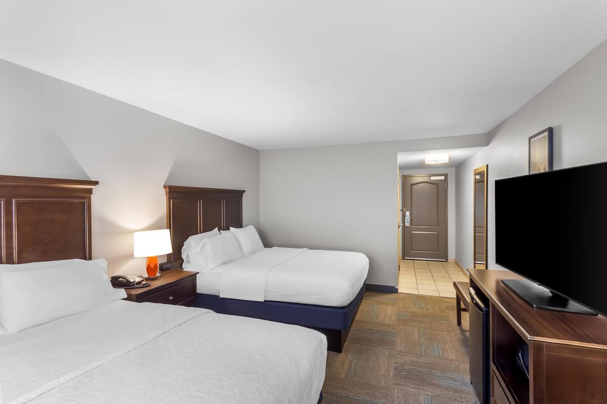 A hotel room with two beds, a television, a desk, and a lamp.