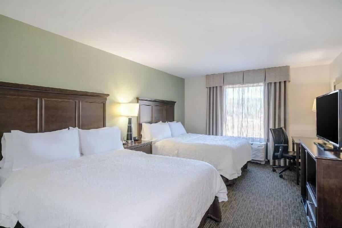 A hotel room with two beds, a desk, a chair, a TV, and a window with curtains.