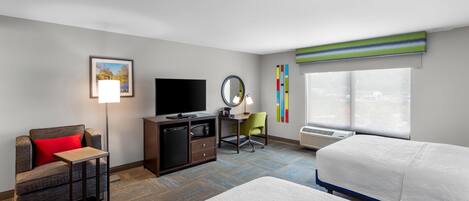 A hotel room with a bed, a desk, a television, a chair, a small table, a mirror, and a window with blinds.