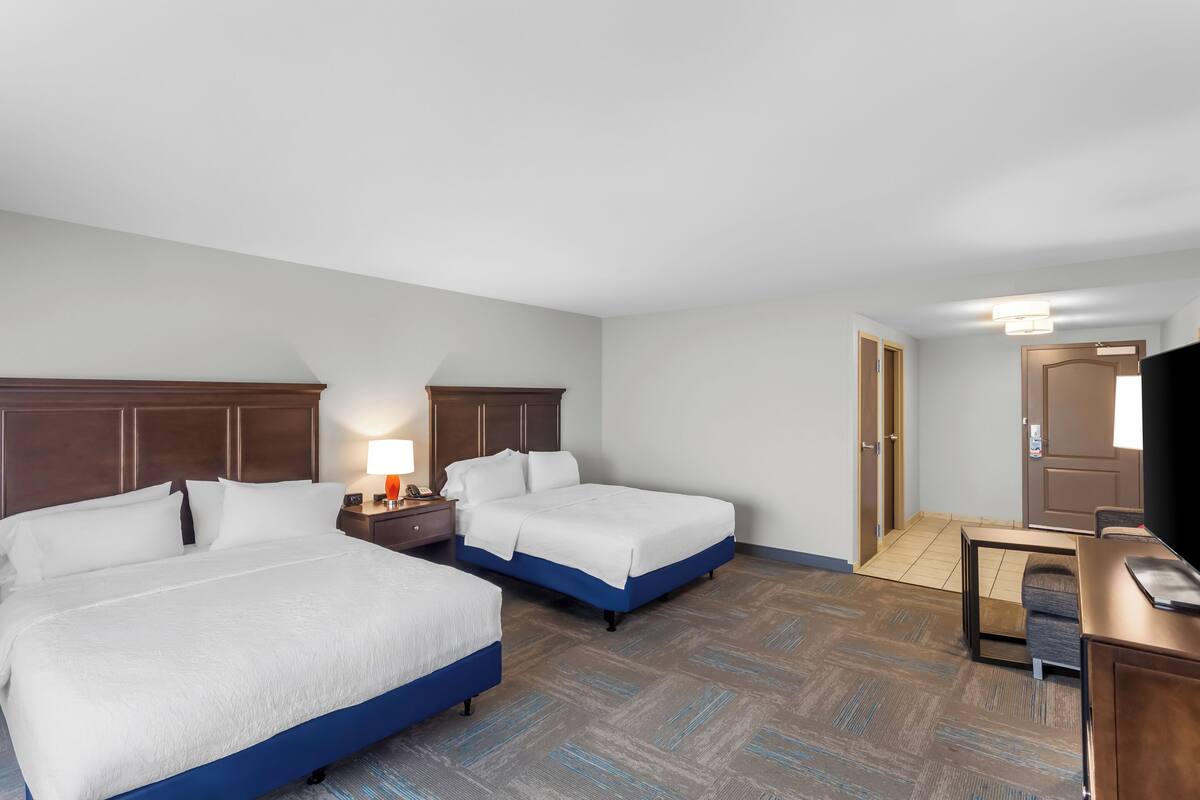 A hotel room with two beds, a desk, a chair, and a television.