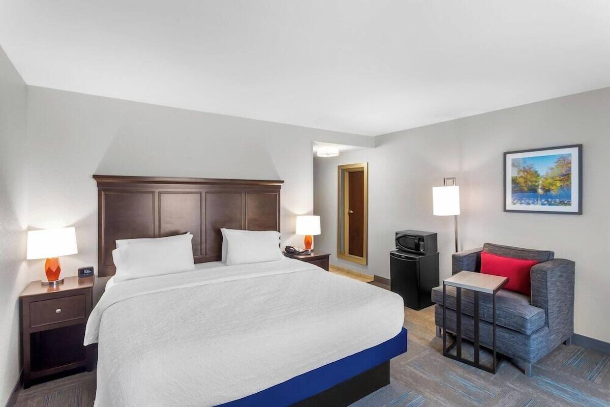 A hotel room with a large bed, a desk with a chair, a TV, and a painting on the wall.