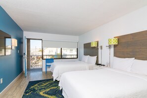 Habitación de hotel con dos camas, un ventanal grande y vistas a la ciudad.
