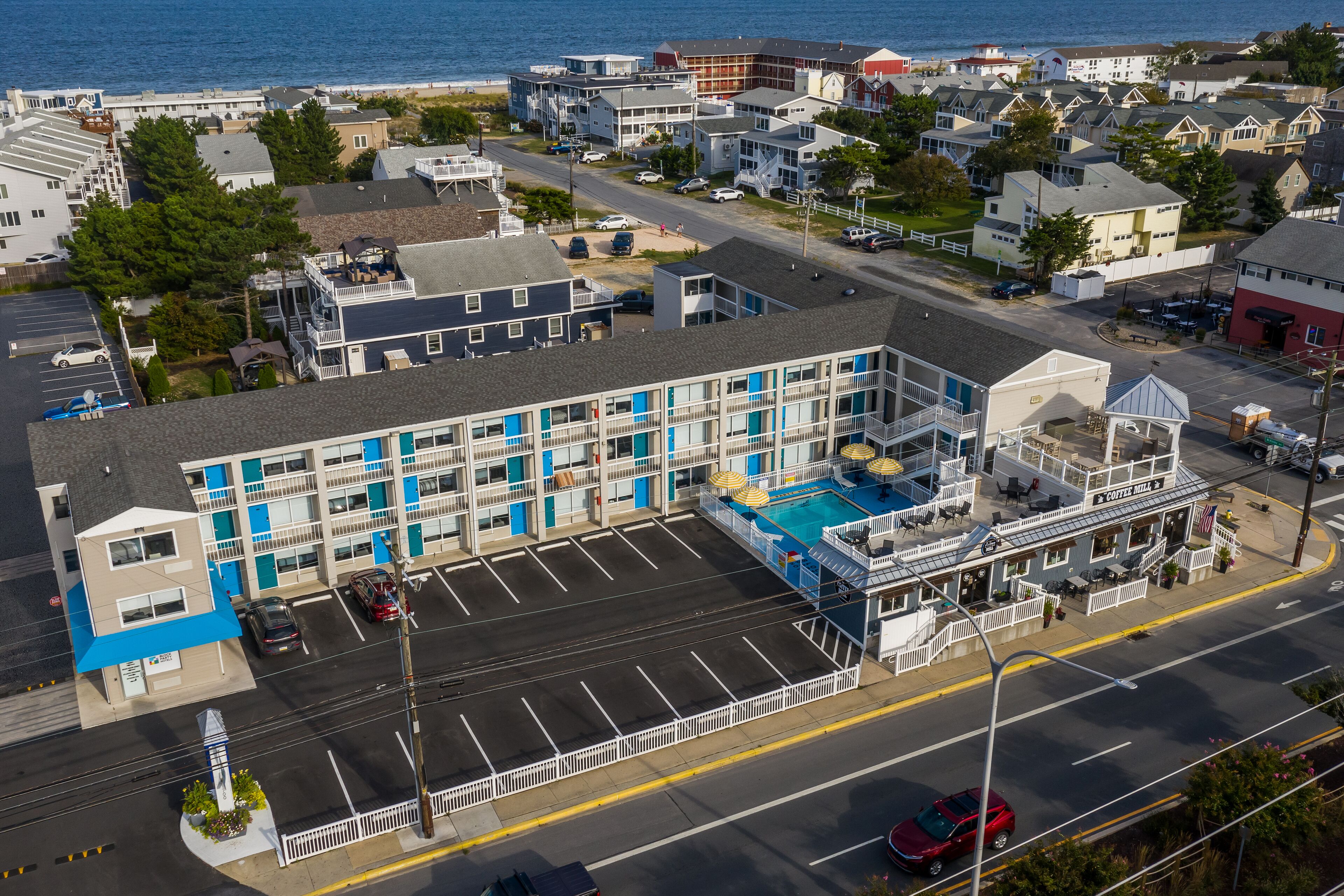 Vista aérea de un hotel frente al mar con varios pisos, una piscina y un estacionamiento.