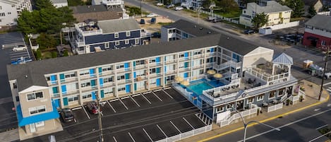 Vista aérea de un hotel frente al mar con varios pisos, una piscina y un estacionamiento.
