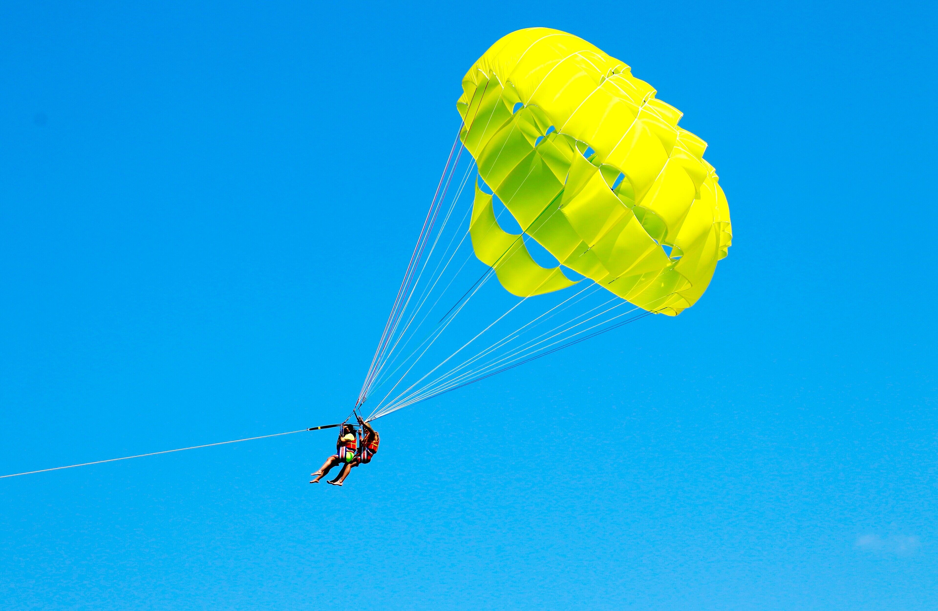 Une personne pratiquant le parachutisme avec un parachute jaune, sur fond de ciel bleu dégagé.