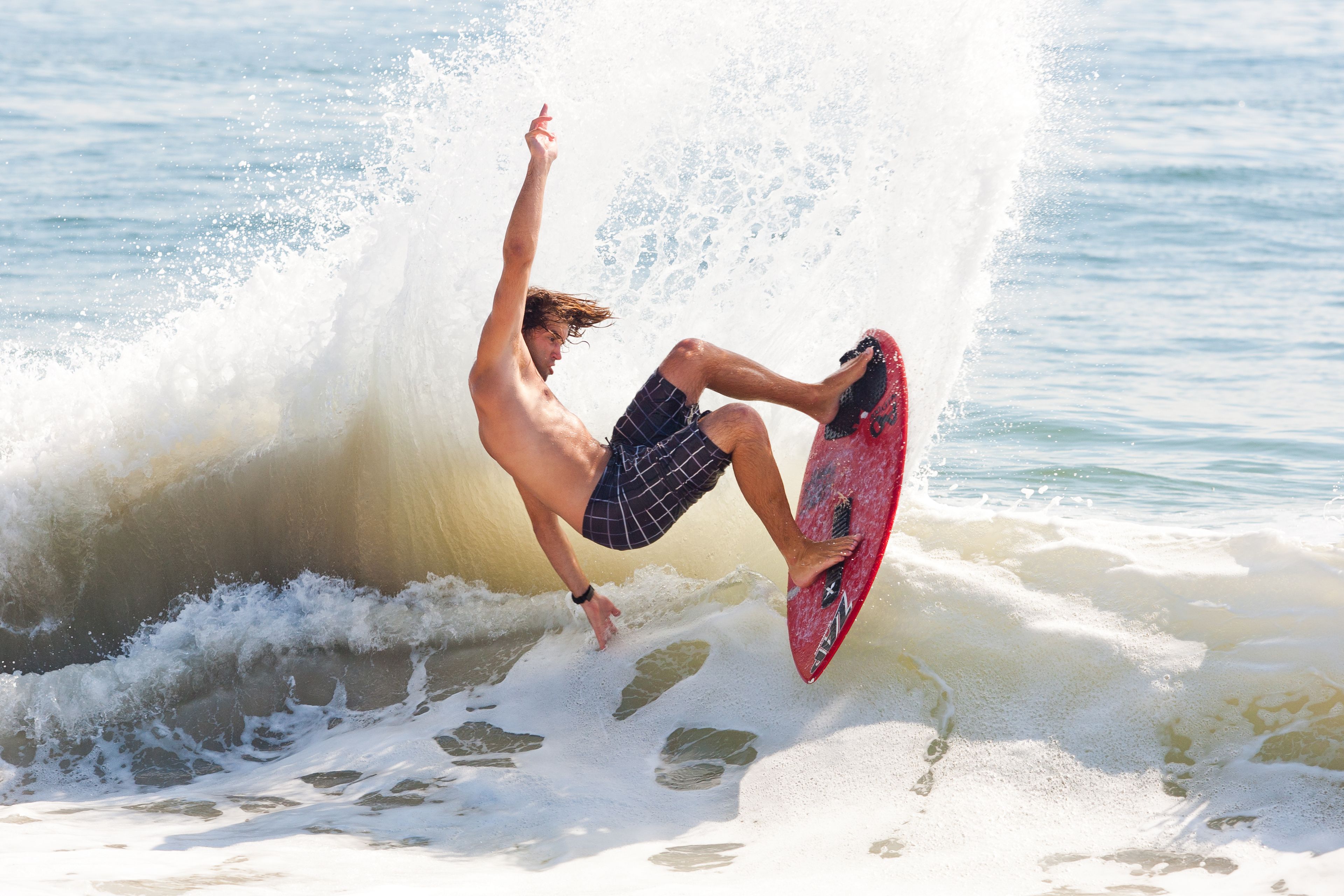 Un surfeur surfe sur une vague avec une planche de surf rouge.
