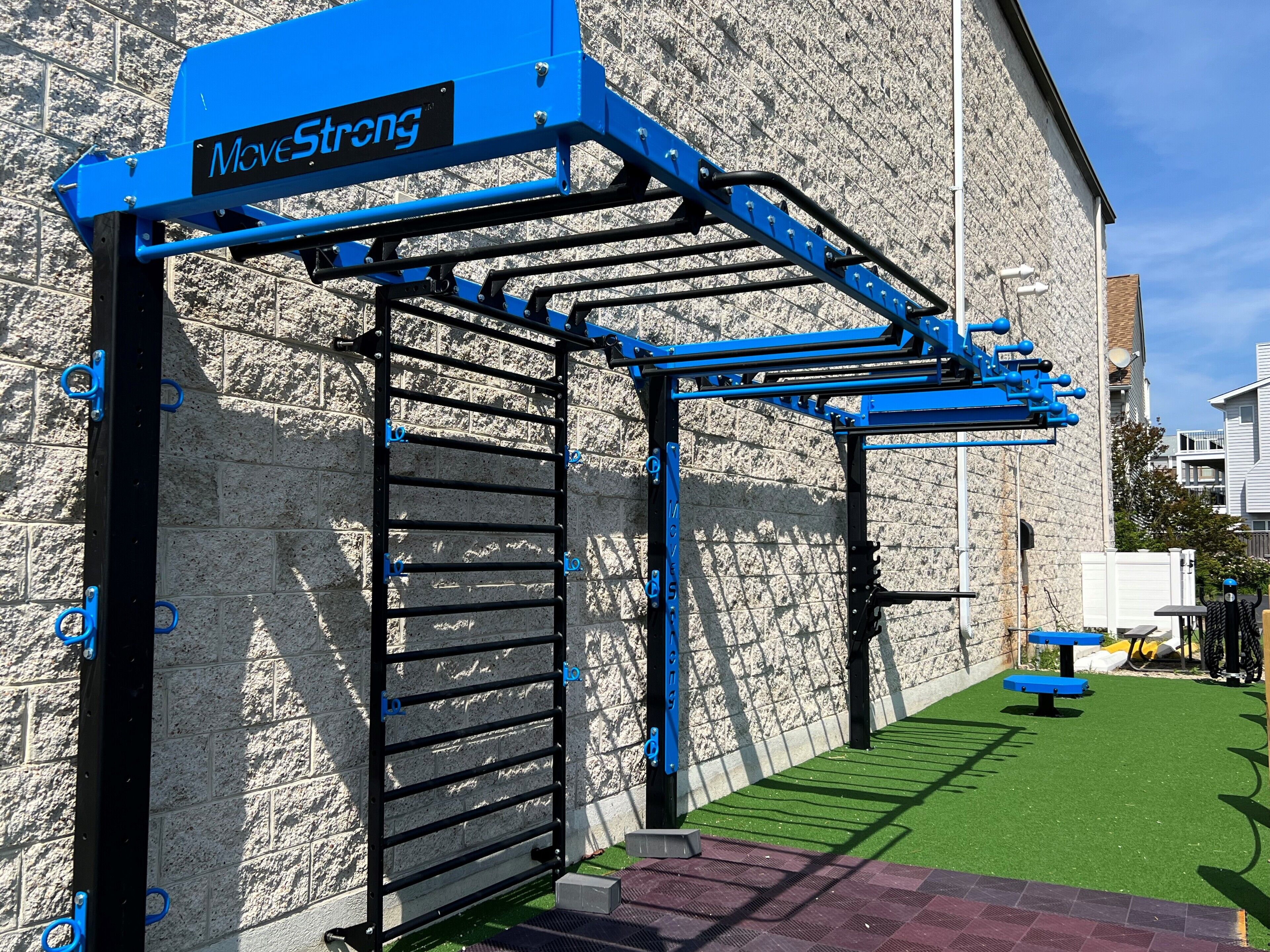 A blue outdoor gym structure with a metal frame and black horizontal bars, attached to a stone wall.