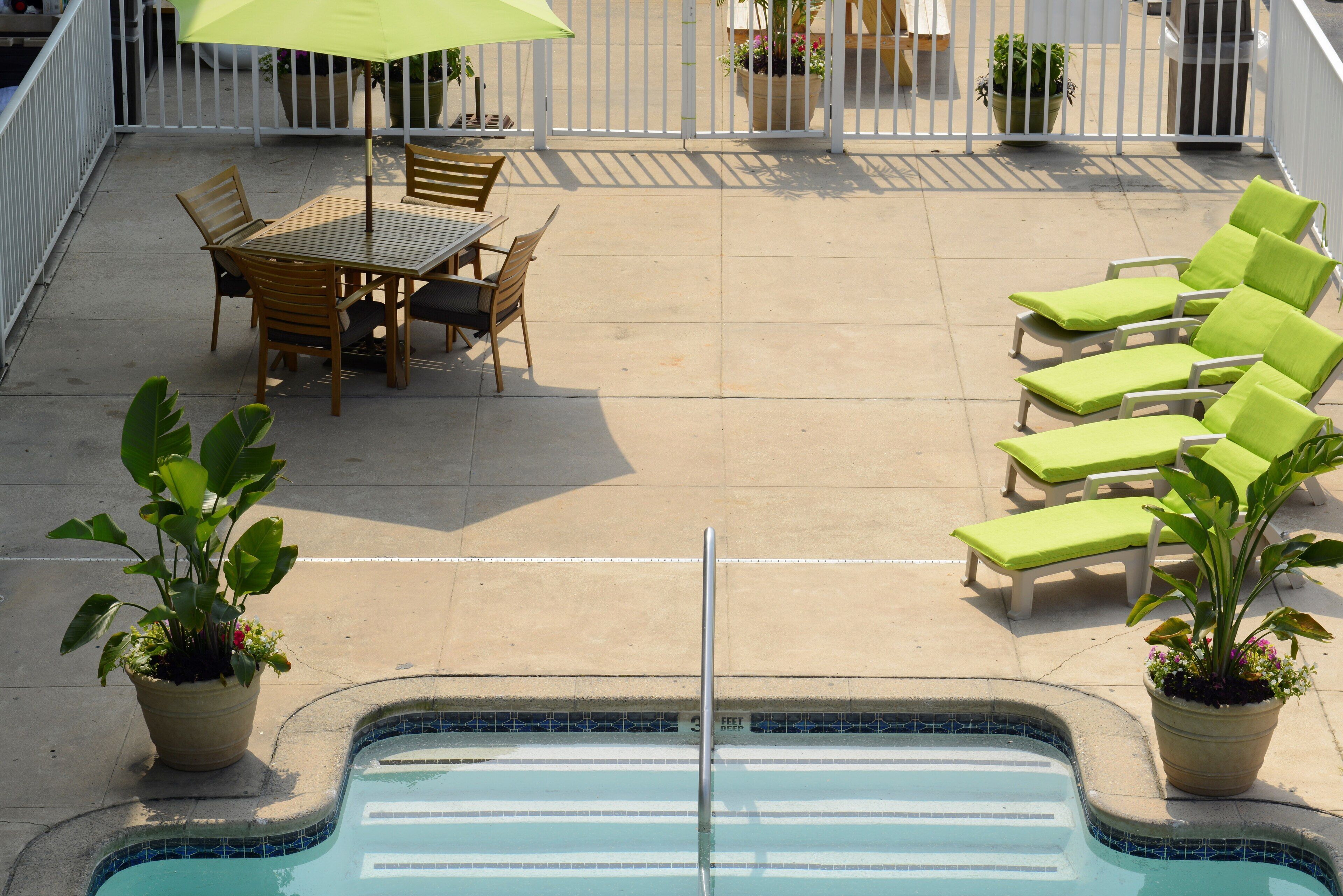 A pool area with a table and chairs, lounge chairs, and potted plants.