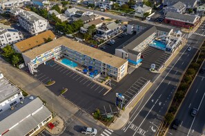 An aerial view of a commercial building with a parking lot, a swimming pool, and multiple floors.