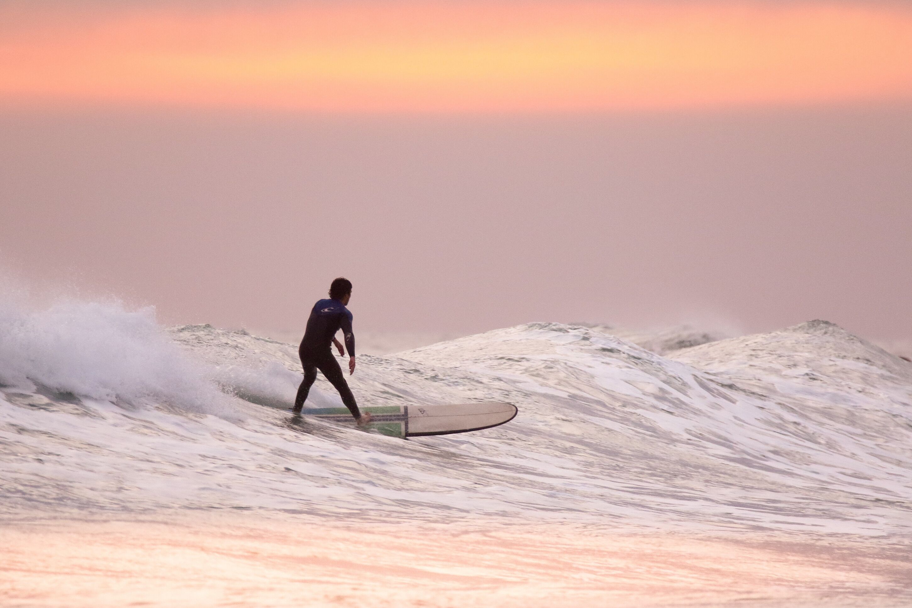 A surfer riding a wave at sunset.