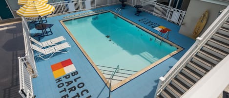 Un área de piscina con sillones de descanso y sombrillas, un puesto de salvavidas y una tabla de surf.