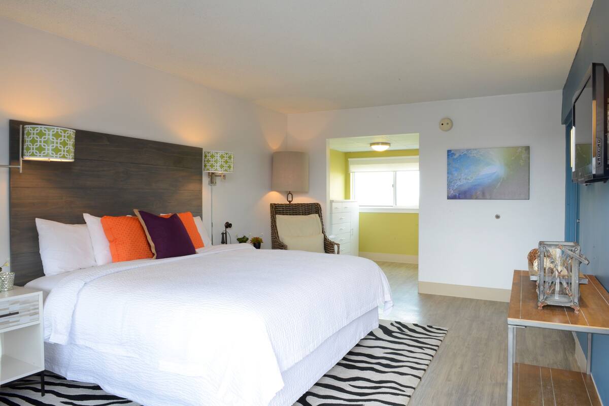 A bedroom with a large bed, a zebra-patterned rug, a chair, a table with a decorative item, and a painting on the wall.