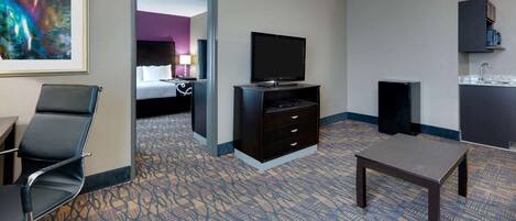 A hotel room with a bed, a desk, a chair, a television, a small table, and a bathroom area.