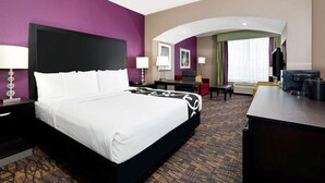 Een hotelkamer met een groot bed, een bureau, een televisie en een zithoek met een stoel en een tafel.