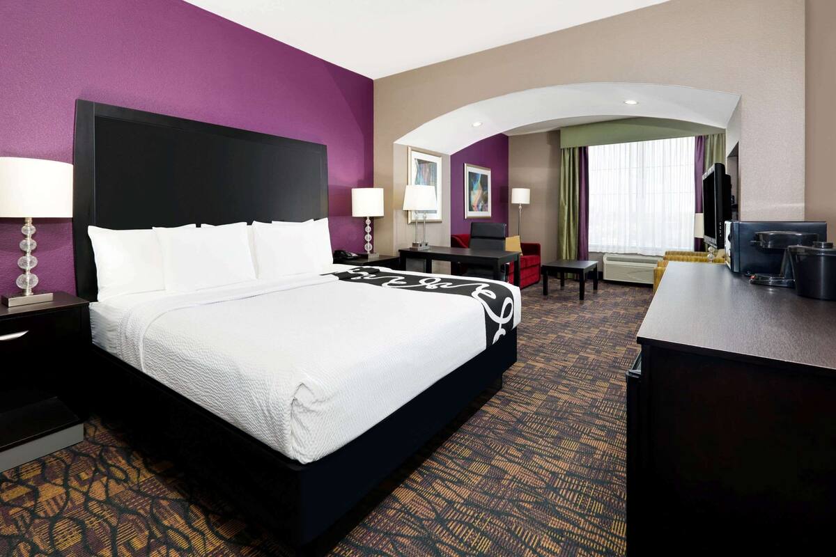 A hotel room with a large bed, a desk, a TV, and a seating area with a chair and a table.