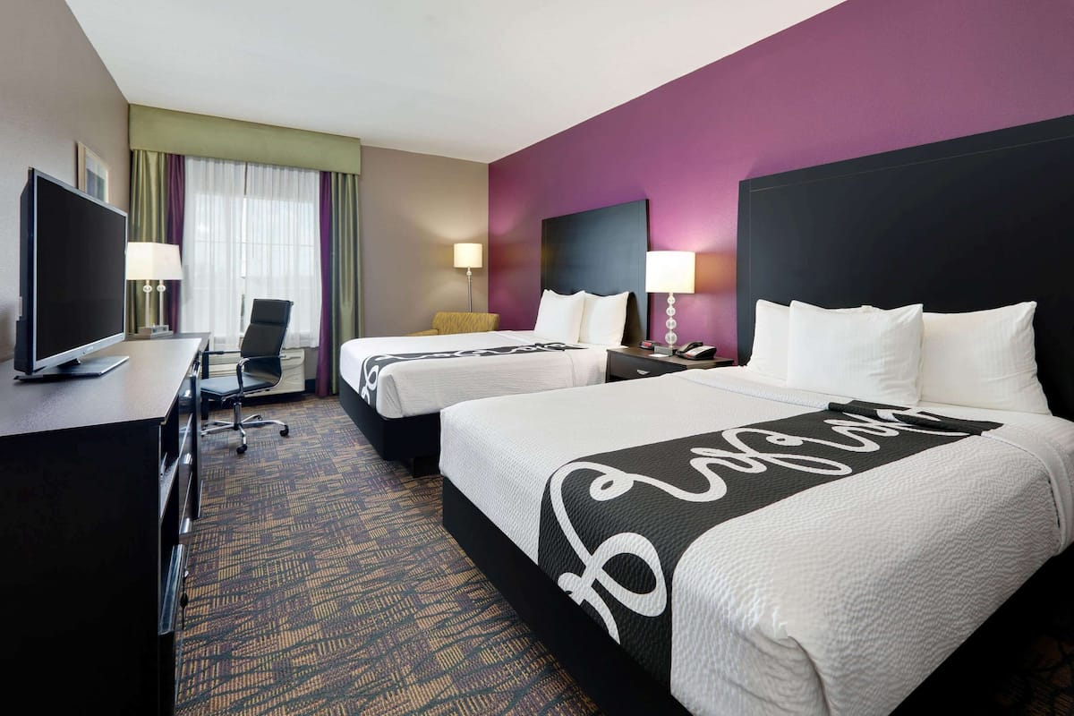 A hotel room with two beds, a desk with a TV, and a chair.