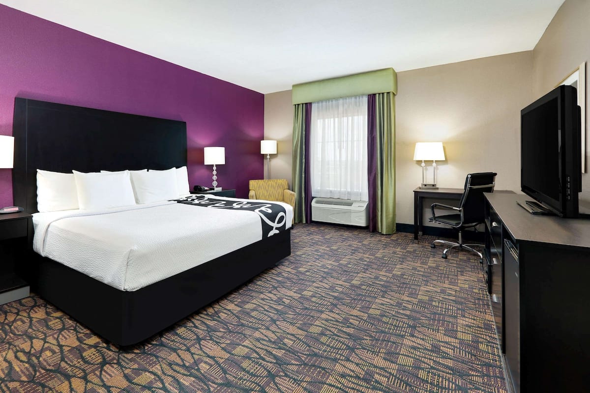 A hotel room with a large bed, a desk with a TV, and a window with curtains.