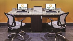 Een vergaderruimte met twee monitoren waarop het logo van La Quinta Inns & Suites staat, een lijst met een abstract schilderij aan de muur en twee bureaustoelen.