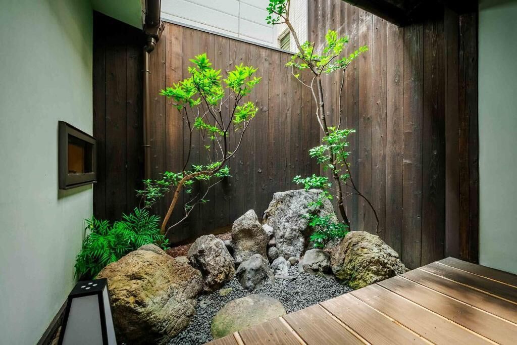 Un jardín japonés tradicional con una mesa de madera, rocas y plantas verdes.