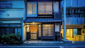 Een traditioneel Japans gebouw met een houten ingang, een pannendak en een kleine tuin met potplanten.