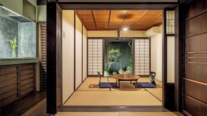 Een traditionele Japanse kamer met tatami vloerbedekking, een lage tafel met kussens en uitzicht op een tuin door een shoji scherm.
