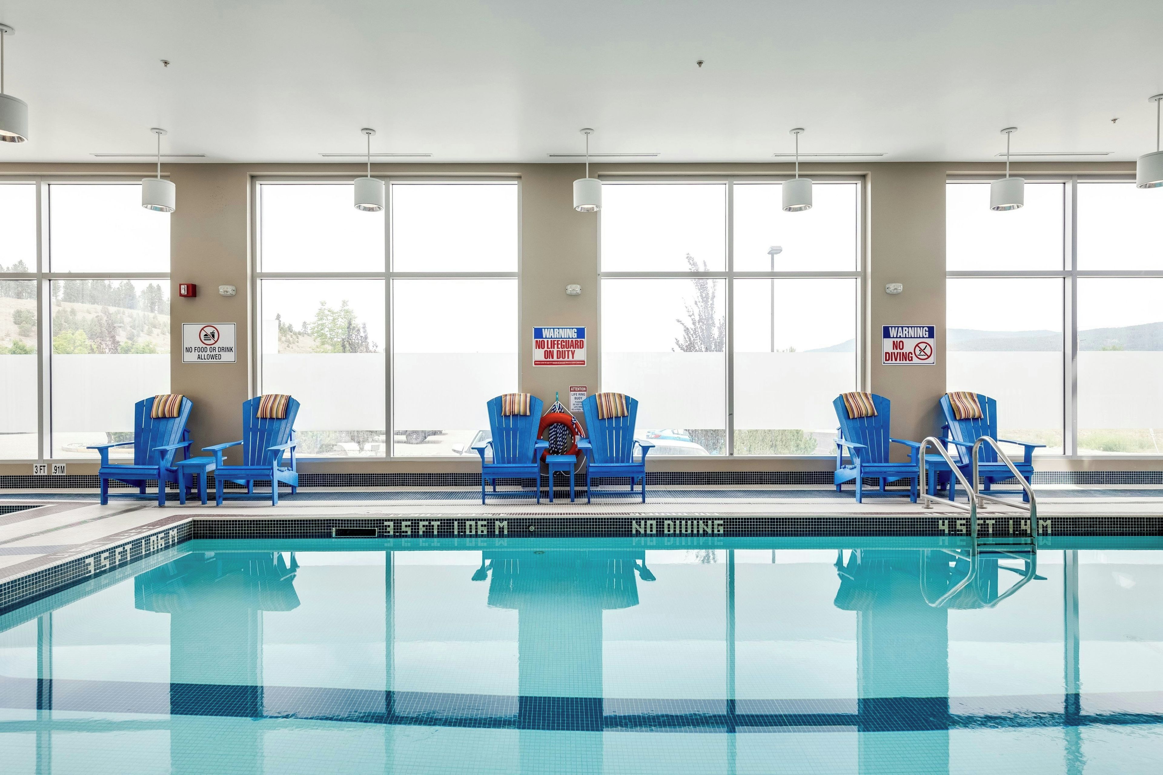 An indoor swimming pool with blue chairs and warning signs.