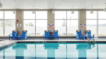 An indoor swimming pool with blue chairs and warning signs.