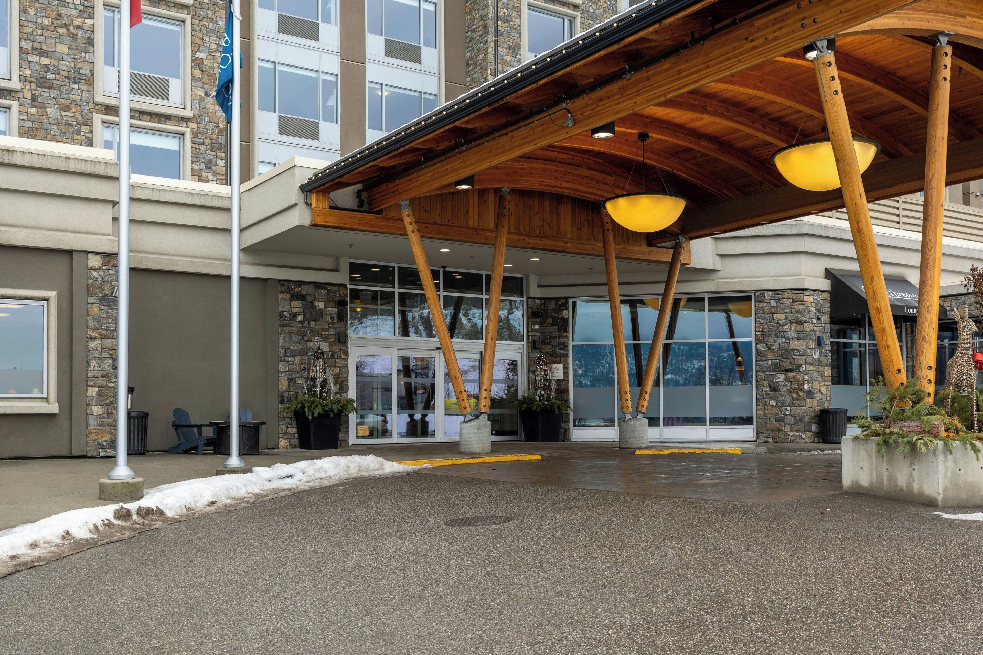 A hotel entrance with a stone facade, large windows, and a covered area with wooden beams and hanging lights.