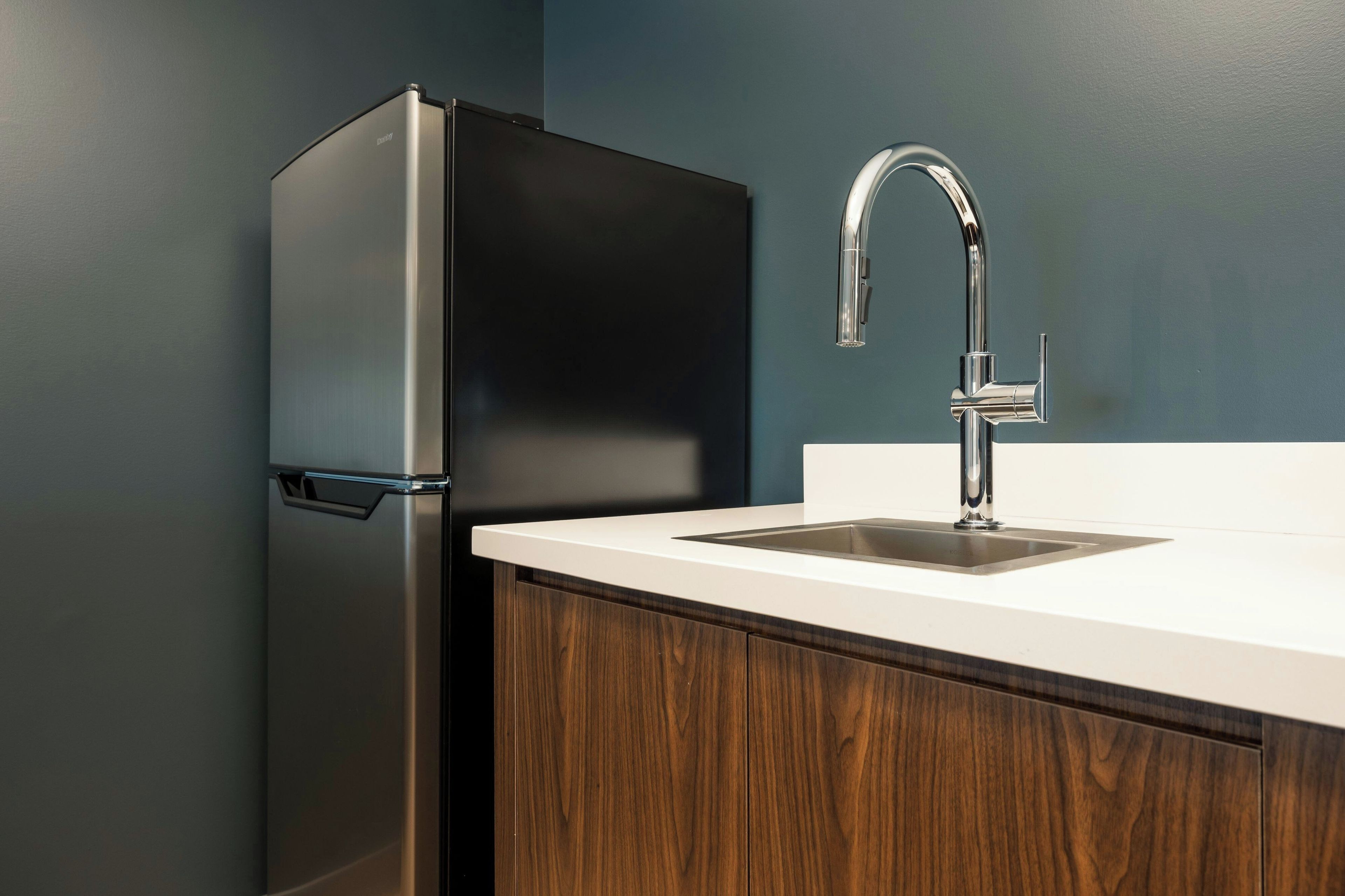 A kitchen with a stainless steel refrigerator, a white countertop, and a modern faucet.