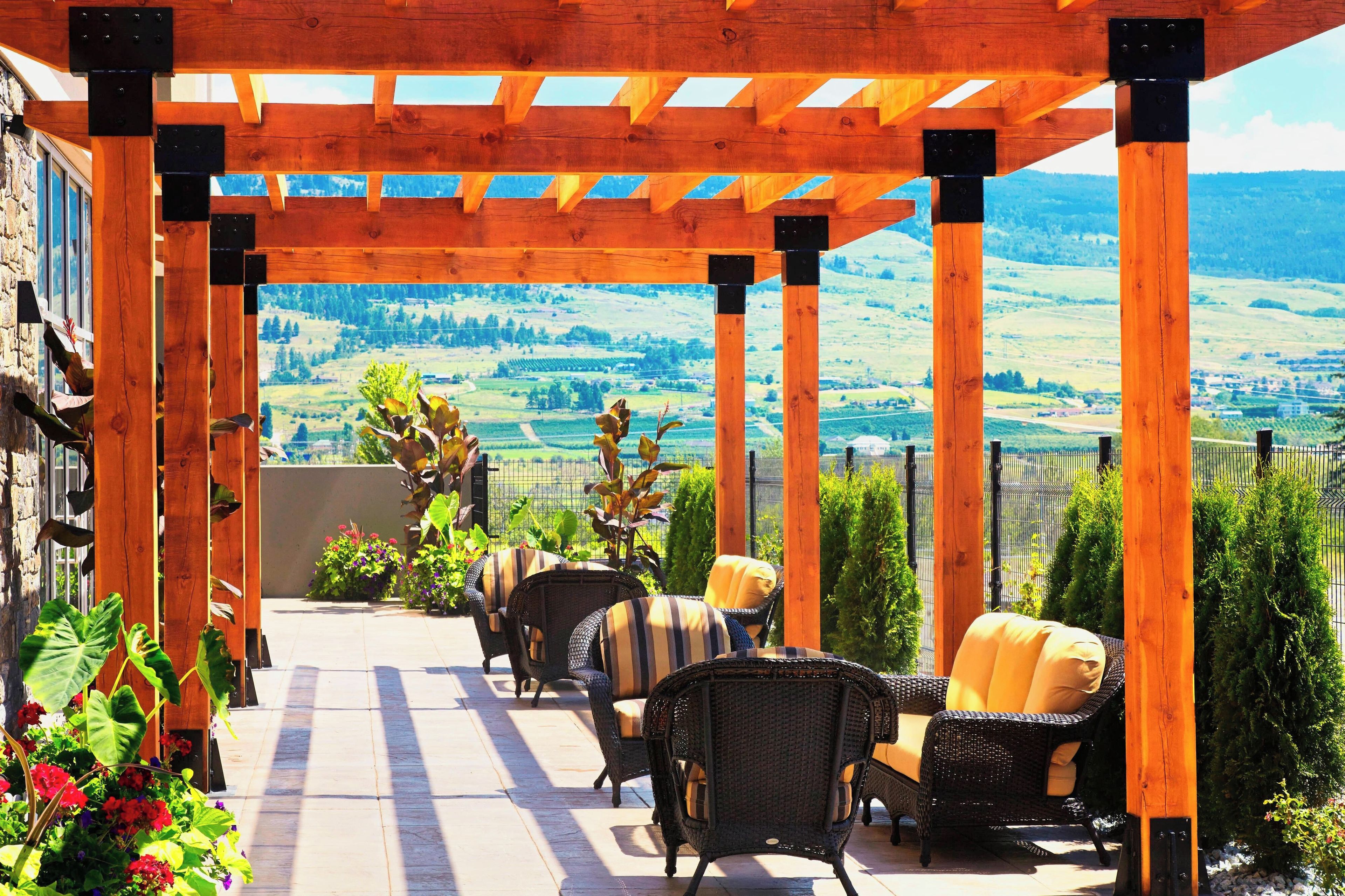 Une terrasse couverte, aménagée avec des meubles en osier, offrant une vue sur un paysage vallonné.