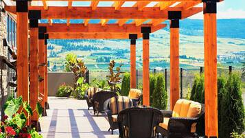 Une terrasse couverte, aménagée avec des meubles en osier, offrant une vue sur un paysage vallonné.