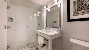 Une salle de bain moderne avec une douche à parois de verre, un lavabo blanc avec un miroir et une œuvre d’art encadrée au mur.