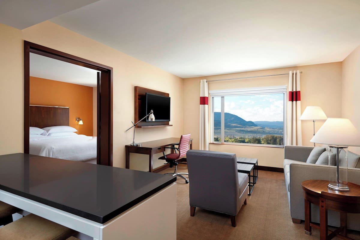 Quarto de hotel com cama, escrivaninha, cadeira, sofá e uma grande janela com vista.