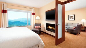 Habitación de hotel con cama, sofá, televisión, chimenea y vistas a las montañas.