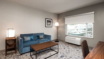 A living room with a blue sofa, a wooden coffee table, a floor lamp, and a large window with a view of a cityscape.