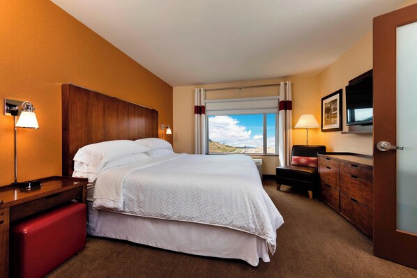 A hotel room with a bed, bedside tables, a dresser, a TV, and a window with a view.