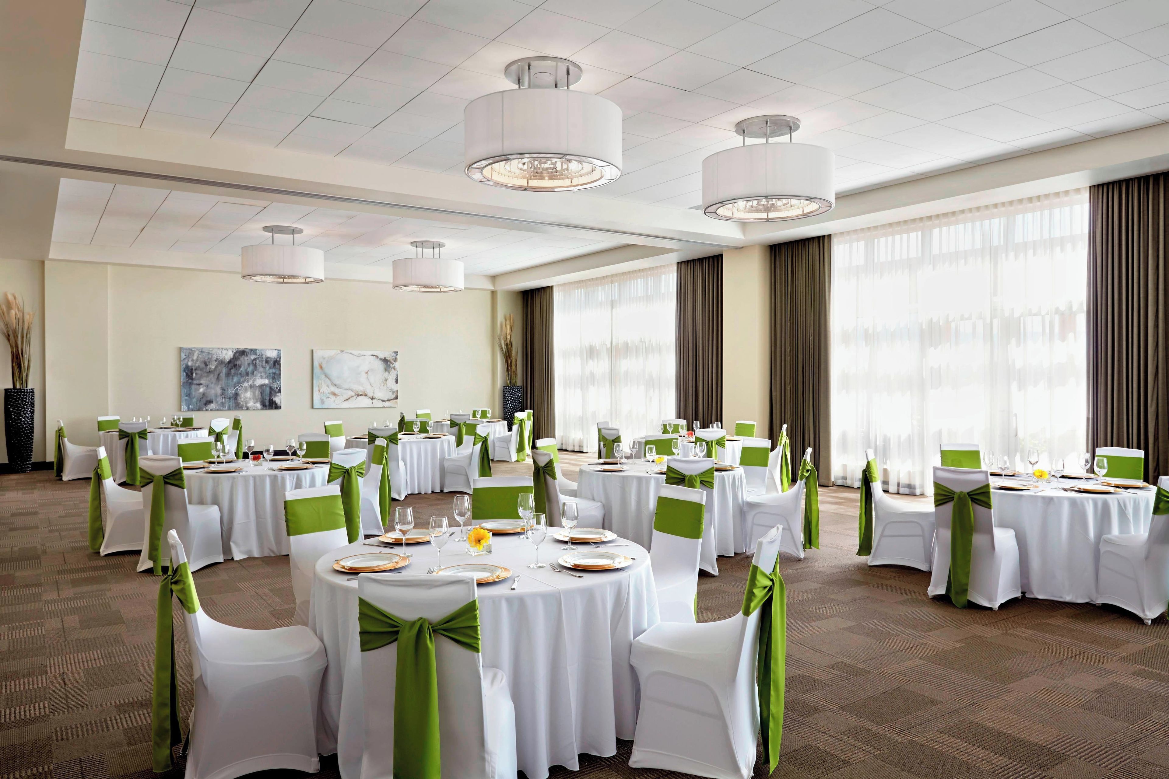 A banquet hall with round tables, white tablecloths, and green sashes on chairs.