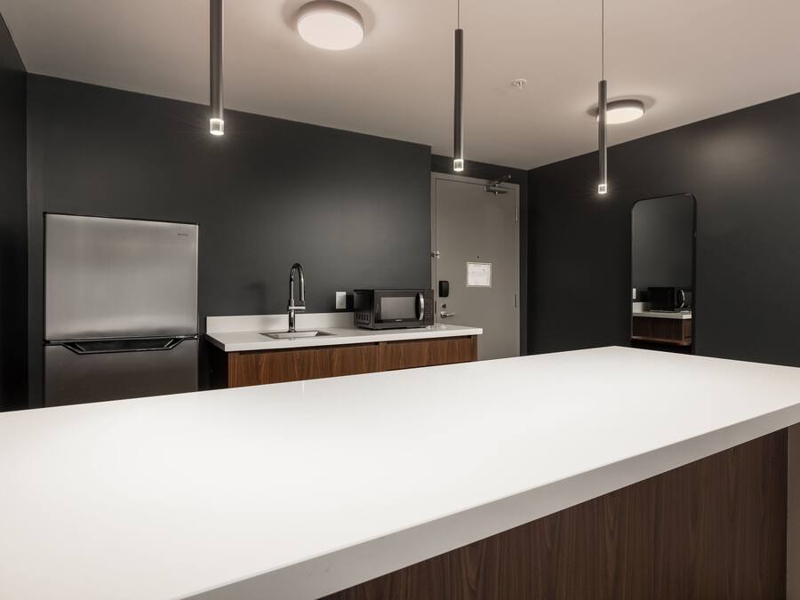A modern kitchen with a white countertop, stainless steel refrigerator, microwave, and a wooden cabinet.