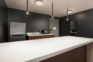 Une cuisine moderne dotée d’un plan de travail blanc, d’un réfrigérateur en acier inoxydable, d’un four à micro-ondes et d’une armoire en bois.