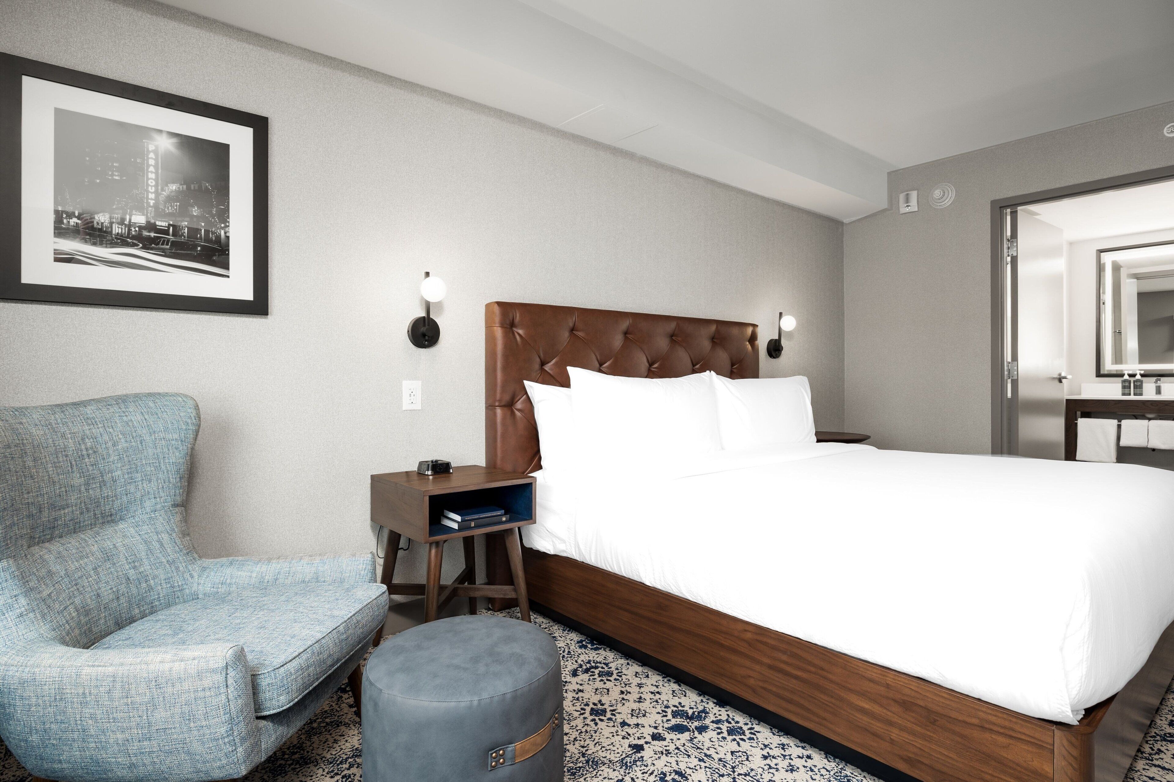 Ein Hotelzimmer mit einem großen Bett, einem Sessel, einem kleinen Tisch und einem Nachttisch.