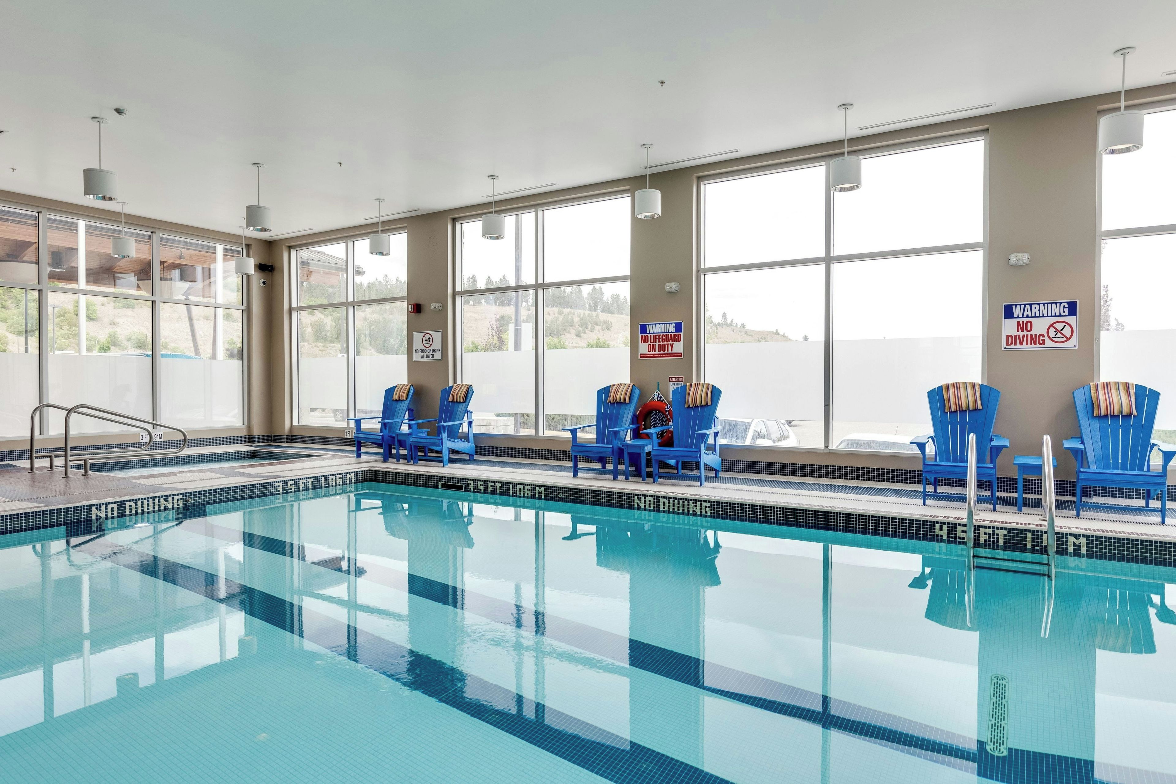 Una piscina interior con sillas azules y un cartel de prohibición de buceo.
