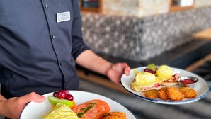 Una persona sosteniendo dos platos con comida, incluyendo huevos benedictinos, croquetas y verduras.